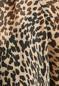 Beige stof met onregelmatige leopardenprint vlekken in donkerbruin en zwart en zichtbare textuurvezels.