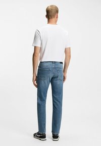 Pantalones vaqueros de mezclilla azul claro con un ajuste slim y diseño de cinco bolsillos, combinados con una camiseta blanca lisa. La vista trasera muestra un acabado impecable.