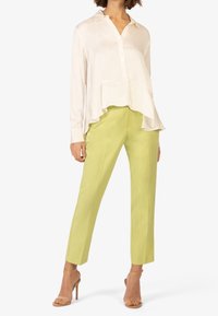 Blusa di seta crema con orlo asimmetrico e colletto, abbinata a pantaloni aderenti verde brillante e décolleté color nude.