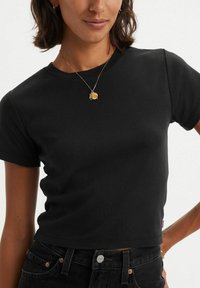 Musta lyhythihainen croppitoppi pehmeästä kankaasta. Yhdistettynä tummiin farkkuihin ja kultaketjuun, jossa on pieni riipus.