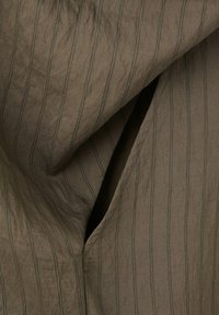 Tissu marron avec de fines rayures verticales noires et des plis superposés visibles créant une ouverture étroite au centre.