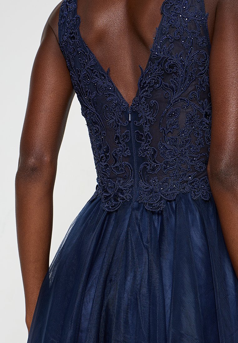 Granatowa suknia z głębokim dekoltem w kształcie litery V i haftem kwiatowym. Przezroczysty gorset przechodzi w warstwową spódnicę z tiulu, z wyszukanym wykończeniem.