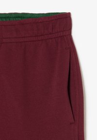 Burgunderfarbene Shorts mit einem gerippten grünen Bund, gefertigt aus strukturiertem Stoff und seitlichen Taschen, verziert mit Nähten entlang der Säume.