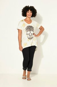 T-shirt blanc à manches courtes avec un design de crâne en imprimé léopard et des accents dorés, associé à un pantalon capri noir avec un ourlet clouté. Sandales argentées.