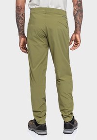 Grüne, leichte, dehnbare Stoffhosen mit passendem Design, sichtbarer Gesäßtasche und verstärkter Naht. Kombiniert mit dunklen Schuhen.