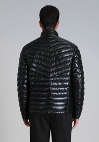 Zwarte pufferjack met een glanzende, gequiltte textuur. Heeft een hoge kraag en een getailleerde silhouette. De achterkant toont een horizontaal stikpatroon.
