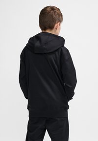Schwarzer Kapuzenpulli mit einer geräumigen Kapuze und langen Ärmeln. Weicher Stoff, schlichtes Design und eine lockere Passform. Kombiniert mit passenden schwarzen Hosen.