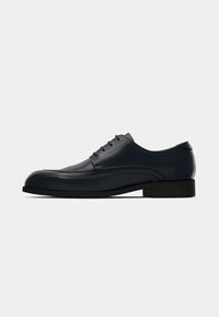 Black leather lace-up men's dress shoe with low heel and stitched detailing on smooth surface.