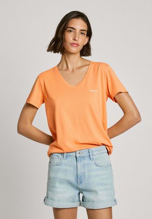 T-shirt arancione con scollo a V e maniche corte, abbinata a pantaloni shorts in denim azzurro arrotolati. Materiale in cotone morbido.
