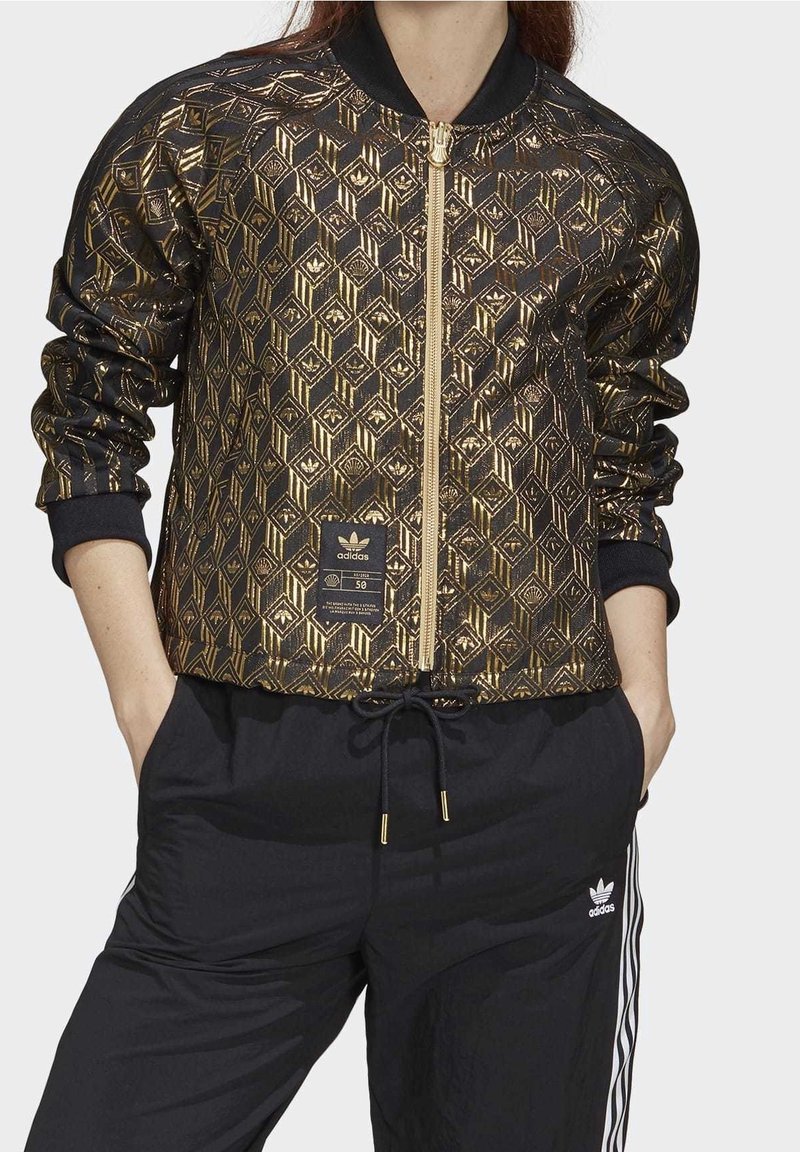 Černá bomber bunda s geometrickým zlatým vzorem, vybavená předním zipem, žebrovanými manžetami a štítkem s logem značky na dolní části předního dílu.