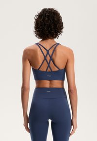 Marineblå sport-bh med korsade axelband, tillverkad av ett mjukt tyg. Har en logotyp bak, i kombination med högmidjade matchande leggings.