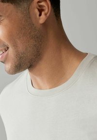 T-shirt in cotone grigio chiaro con girocollo e maniche corte, caratterizzata da un'ottima cucitura e una superficie liscia. Focus sul collo e sulla parte superiore del torso.