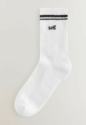 Baltas kokvilnas zeķes ar melniem svītrām augšpusē un melnu uzrakstu "self". Audumam ir ribota struktūra.