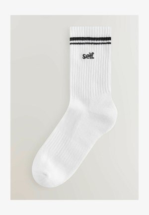 Baltas kokvilnas zeķes ar melniem svītrām augšpusē un melnu uzrakstu "self". Audumam ir ribota struktūra.