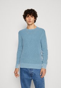 Hellblauer gestrickter Pullover mit einem strukturierten Muster und geripptem Saum. Kombiniert mit lockeren Denim-Jeans, die ein einfaches Rundhalsdesign aufweisen.