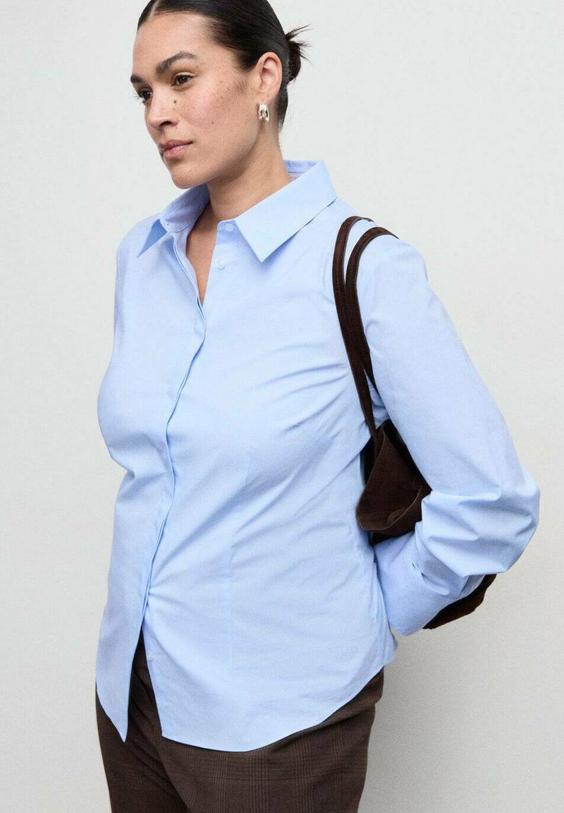 Svetlomodrá košeľa na gombíky s klasickým golierom, dlhými rukávmi a hladkou textúrou, skombinovaná s hnedými nohavicami a hnedou taškou cez rameno.