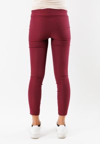 Pantaloni aderenti bordeaux realizzati in tessuto elasticizzato, con vita alta e senza tasche visibili. Indossati con sneakers bianche.