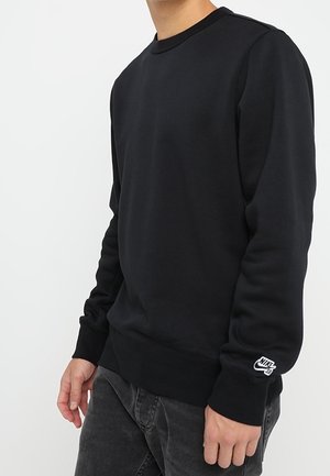 Sudadera negra de cuello redondo hecha de una mezcla de algodón, con puños y dobladillo acanalados. Pequeño logo blanco de Nike en la manga izquierda.