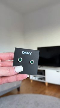 Runde grüne Ohrringe mit funkelnden klaren Akzenten, auf einer schwarzen DKNY-Karte befestigt. Das Material scheint metallisch mit einer strukturierten Oberfläche zu sein.