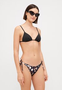 Black triangle bikini top with thin straps paired with tie-side bikini bottoms featuring a multicolored abstract pattern.