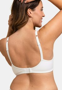Soutien-gorge blanc avec bretelles ajustables, une texture lisse et une fermeture à crochets. Des accents circulaires améliorent le design des bretelles.