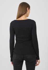 Schwarzes geripptes Langarmtop mit weitem Ausschnitt, figurbetontem Schnitt und weichem Material. Kombiniert mit dunklen Jeans, die ein einfaches Design zur Schau stellen.