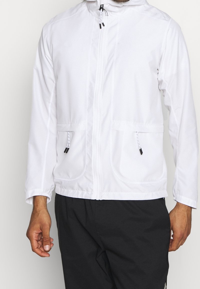 Chaqueta blanca con capucha que presenta un cierre frontal, dos bolsillos delanteros, cintas ajustables y puños elásticos para un ajuste seguro.