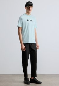 Helehall sinine lühikeste varrukatega T-särk musta "BOSS" logoga; mustad püksid; mustad tossud; must nokamüts tikandiga logoga.