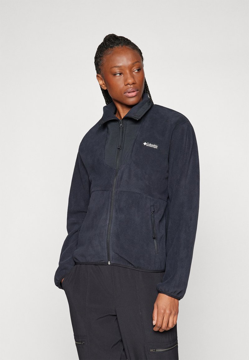 Zippered navy fleece jacket with long sleeves, high collar, and two side pockets; features a contrasting panel at the chest and logo detail.