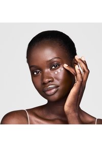 Modell mit dunkler Haut, der eine Creme auf den Bereich unter den Augen aufträgt; besitzt eine glatte Textur, natürlichen Glanz und minimalistische Styling.