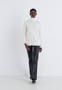 Cream turtleneck sweater with ribbed hem, paired with fitted black faux leather flared pants, creating a sleek silhouette.