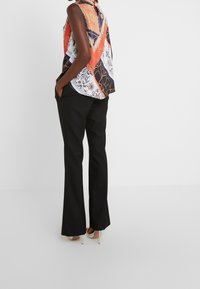 Mouwloze multikleurige blouse met een geometrisch en bloemmotief, gecombineerd met zwarte flared broek en beige hoge hakken.