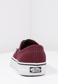 Bordeaux canvas Vans sneakers med låg profil, vit gummisula och svarta accenter. "OFF THE WALL"-logotyp synlig på hälen.