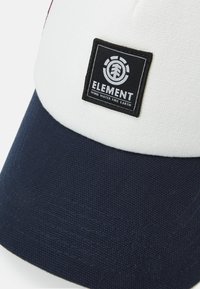 Kappe med hvit topp og mørk marineblå skjerm, laget av teksturert stoff; inkluderer et svart ELEMENT-logo patch foran.