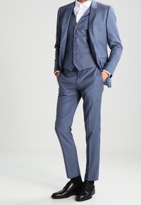 Traje de tres piezas azul claro con un diseño ajustado, que presenta solapa de muesca, tres botones en el chaleco y zapatos de cuero negros.