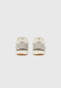 Sneakers Nike z beżową i szaro-tekstylną cholewą, jasnoszarymi akcentami, teksturowanymi detalami na pięcie oraz gumową podeszwą w jasnobrązowym kolorze.
