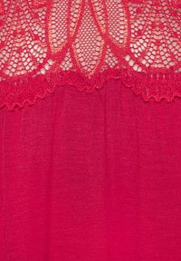 Tessuto rosso con un bordo di pizzo scallopato nella parte superiore, decorato con un motivo floreale e dettagli delicati. La texture è morbida e leggera.