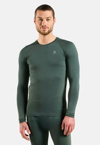 Green long-sleeve thermal top with a textured pattern, crew neckline, and fitted design, made from moisture-wicking material.