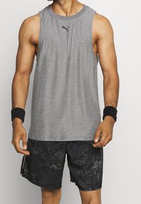 Šedé bezrukávové sportovní tričko s jemným logem na hrudi, spolu s černými šortkami s texturovaným vzorem a bočním zipovým kapsičkou.