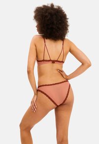 Vahanen pitsireunuksin varustettu burgundinpunainen liivi ja alushousut pehmeästä beigen värisestä kankaasta; sisältää säädettävät hihnat ja takana olevan hakaskiristyksen.