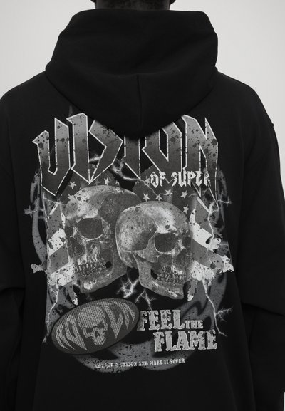 Sweat à capuche noir avec un graphisme audacieux "VISION" comprenant des skulls, des motifs d'éclairs et le texte "RESSENTIR LA FLAMME" imprimé en blanc. Texture douce.
