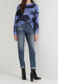 Světle modrý nadýchaný svetr s černým květinovým vzorem, zkombinovaný se zúženými modrými džíny a černými vysokými kotníkovými botami.