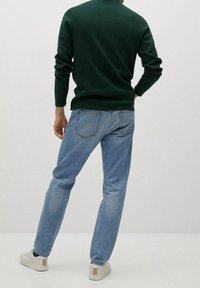 Grüner Strickpullover, blaue gerade Jeans und weiße Sneakers mit beigen Akzenten. Ansicht von hinten, mit Fokus auf die Kleiderdetails und -texturen.