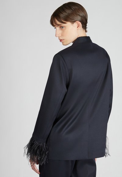 Granatowa marynarka o eleganckim kroju, z teksturowanymi piórami w akcentach mankietów. Gładka, wykończona tkanina z dopasowanym krojem i minimalistycznym kołnierzykiem.