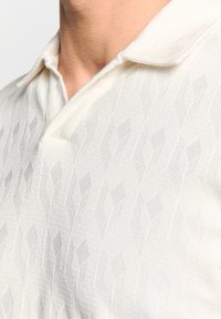 Witte polo met een gekruist diamantpatroon, voorzien van een kraag en korte mouwen, gemaakt van een zachte katoenachtige stof.