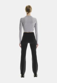 Hellgrauer, langärmeliger, enganliegender Crop-Top mit Rundhalsausschnitt, kombiniert mit hoch taillierten schwarzen Hosen, von hinten betrachtet. Schwarze Schuhe sind sichtbar.