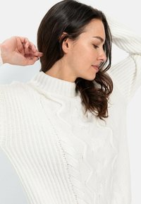 Weißer gestrickter Pullover mit hohem Stehkragen und Zopfmuster, mit gerippter Textur und lockerer Passform.