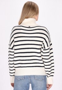 Sweater a righe in crema e nero, con collo alto, texture a coste e dettaglio con bottoni sul retro. Vestibilità ampia e oversize.