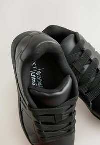 Chaussures de sport noires avec une tige en cuir lisse, des lacets noirs texturés et un col rembourré, bénéficiant de la marque Ortholite à l'intérieur.