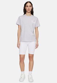 T-shirt in cotone viola chiaro con maniche corte e colletto rotondo; presenta un logo bianco sul petto. Abbinato a pantaloni corti da bicicletta bianchi a costine.